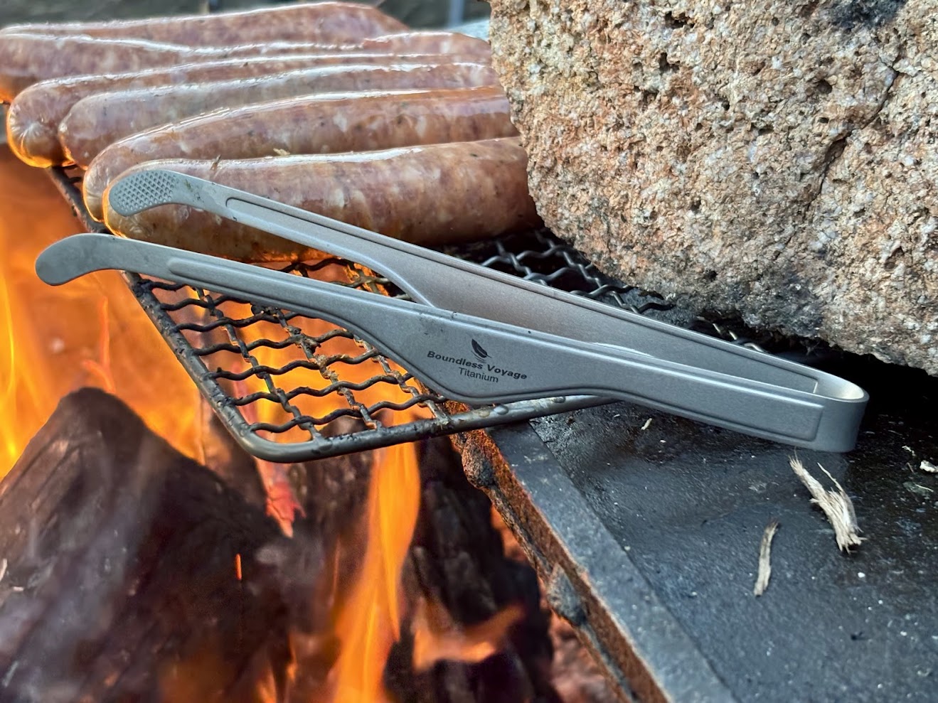 Using the Boundless Voyage titanium tongs​ to flip sausages over the campfire