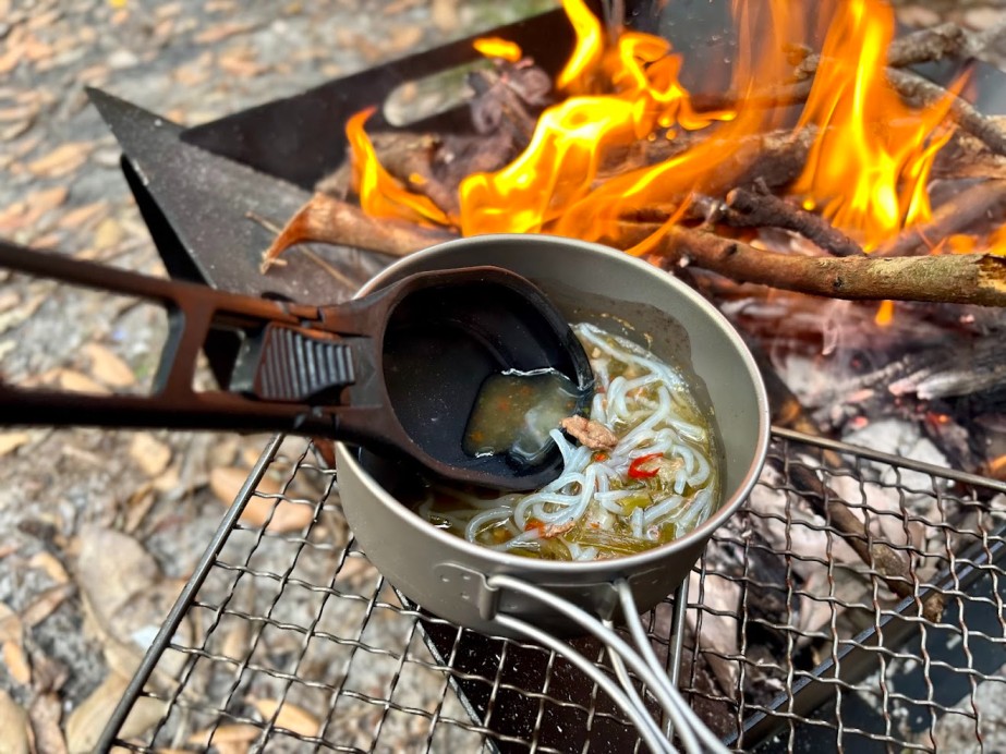 Using a small titanium grill plate over the Adventure Kings portable steel fire pit​ to heat up small dishes