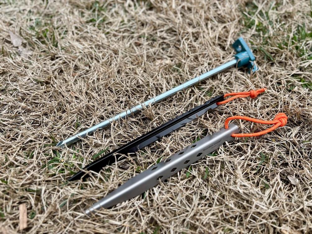 Comparing the size of a standard black steel tent peg, the long Coleman steel tent stakes (120g) and the Boundless Voyage titanium tens pegs (23g)