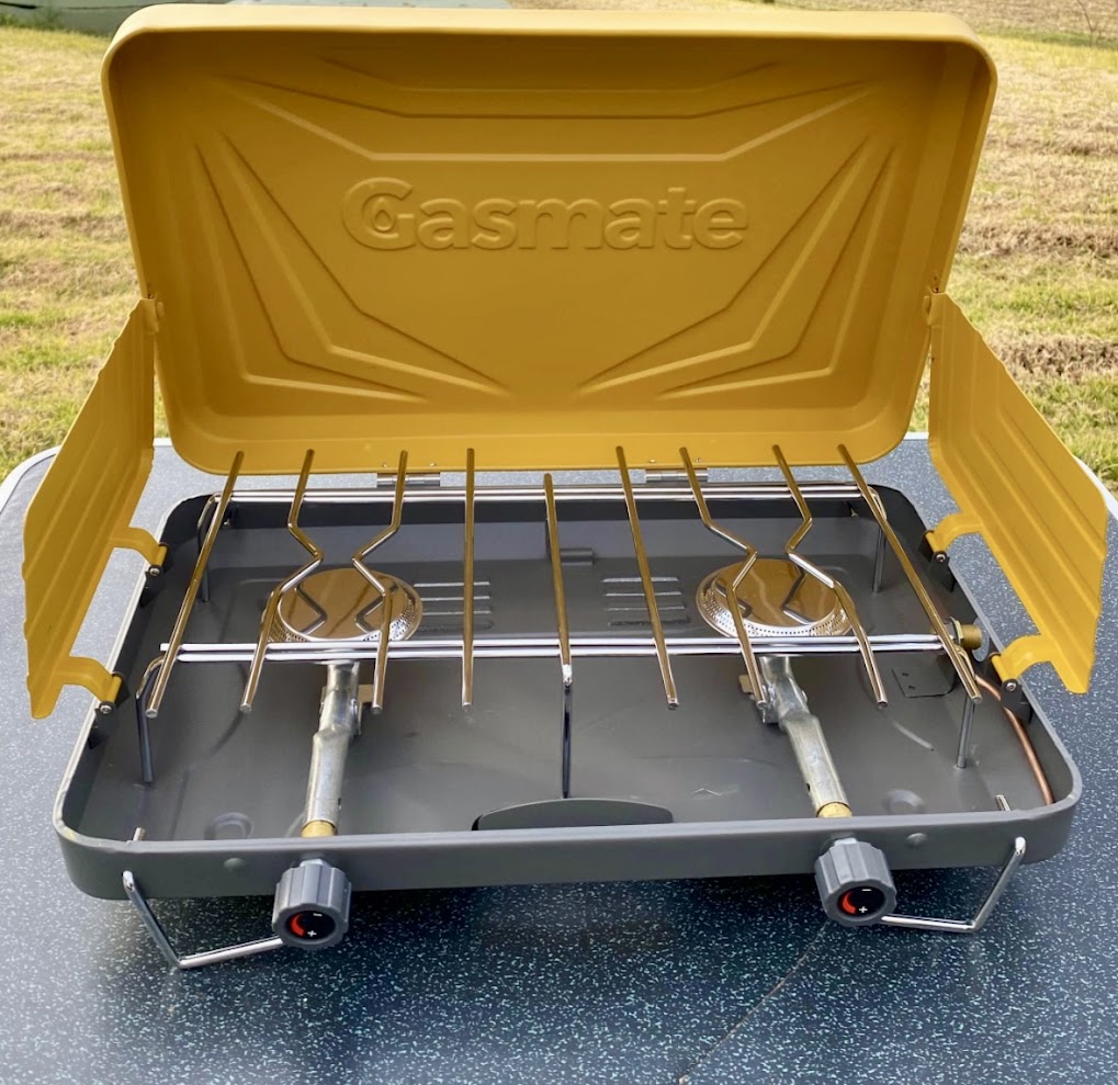 The lid of the Gasmate 2 burner stove lifts and locks into place, forming the essential rear windshield, while the side flaps swing out for extra wind protection